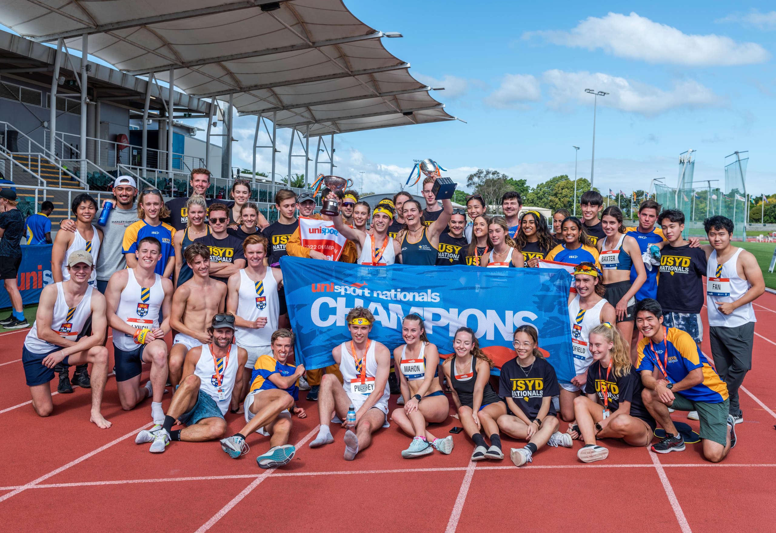Large group of The University of Sydney students gathered posing with 'champions' banner at Nationals Athletics competition.
