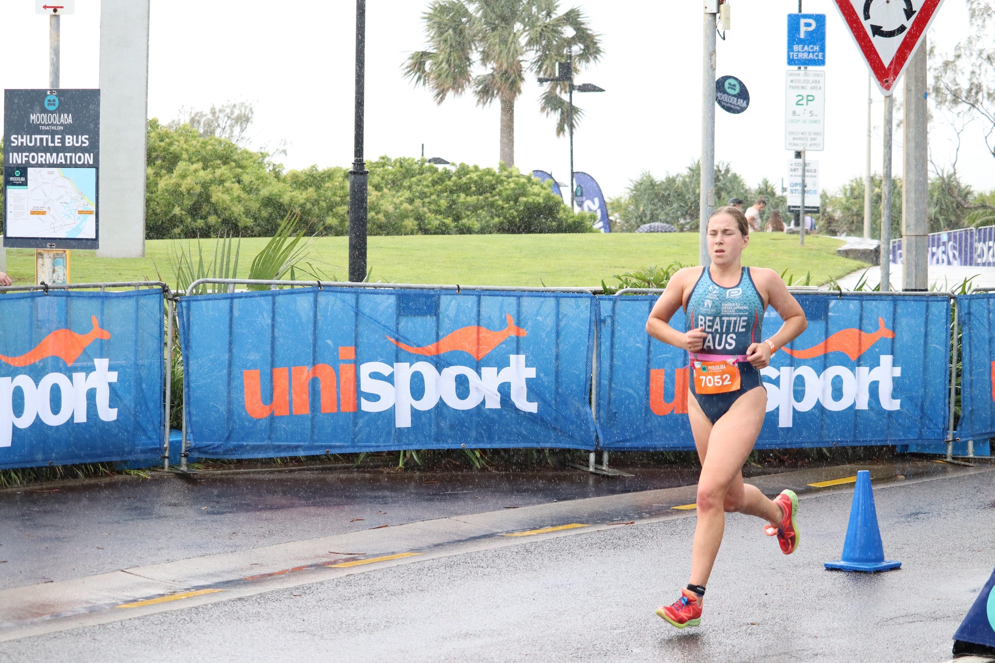 Female athlete running in rain in front of UniSport signage..