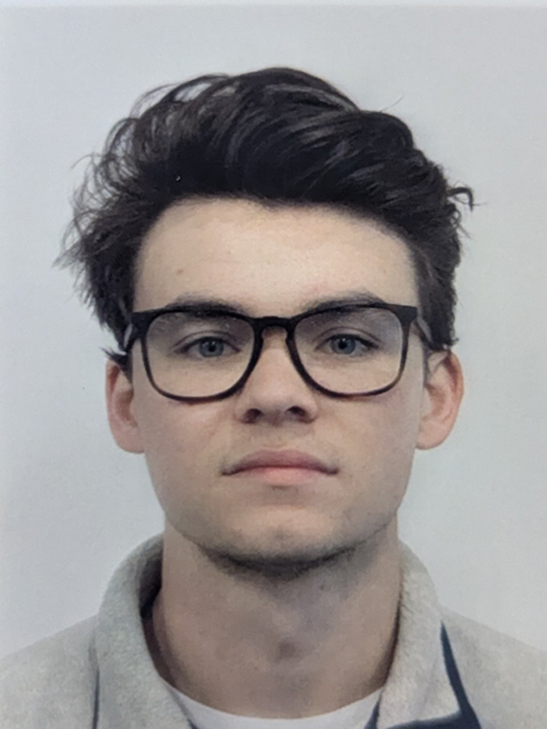 Portrait of a young man with dark hair and black rectangular glasses, looking straight at the camera.