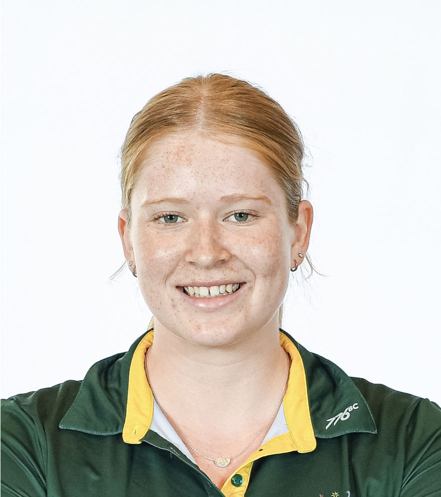 Smiling young woman with red hair tied back, wearing a green and yellow polo shirt.