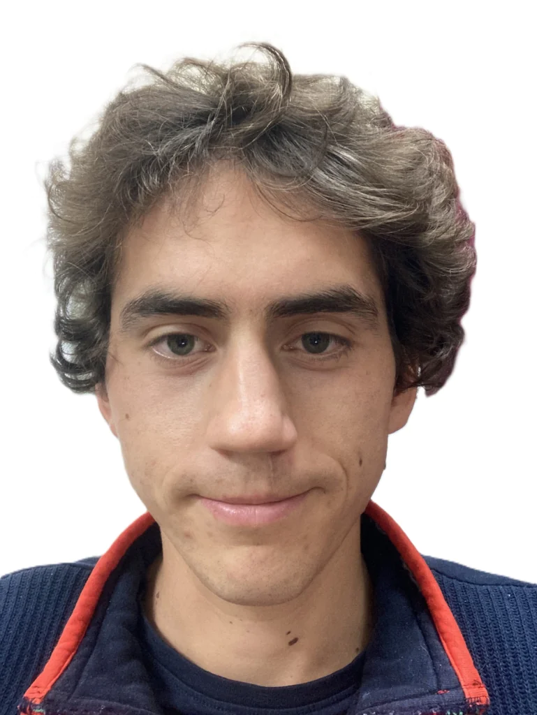 Close-up of a young man with wavy dark hair and blue-green eyes, wearing a navy sweater with red trim.