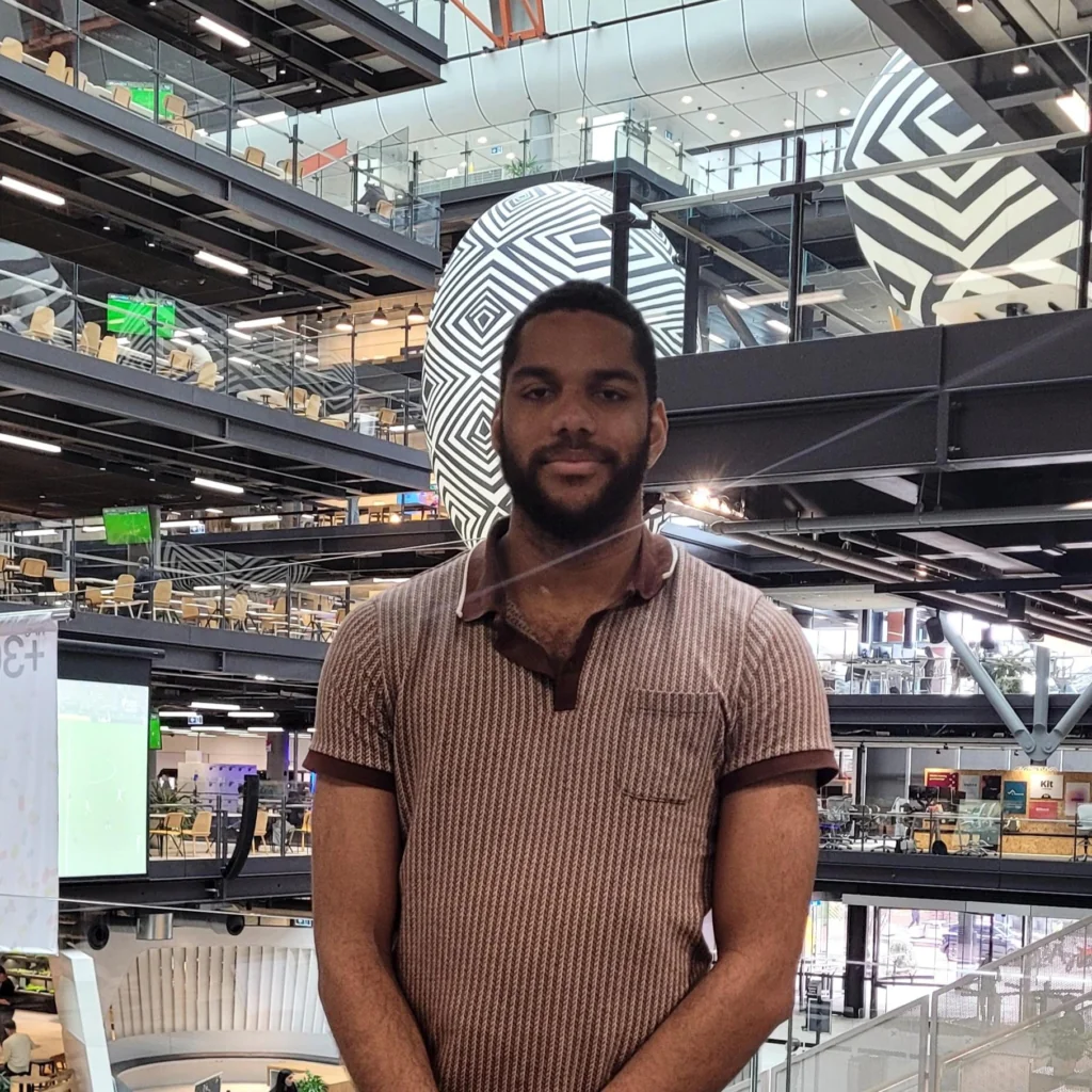 Man in a brown striped polo standing in a modern multi-level atrium with a large black-and-white geometric sculpture behind him.