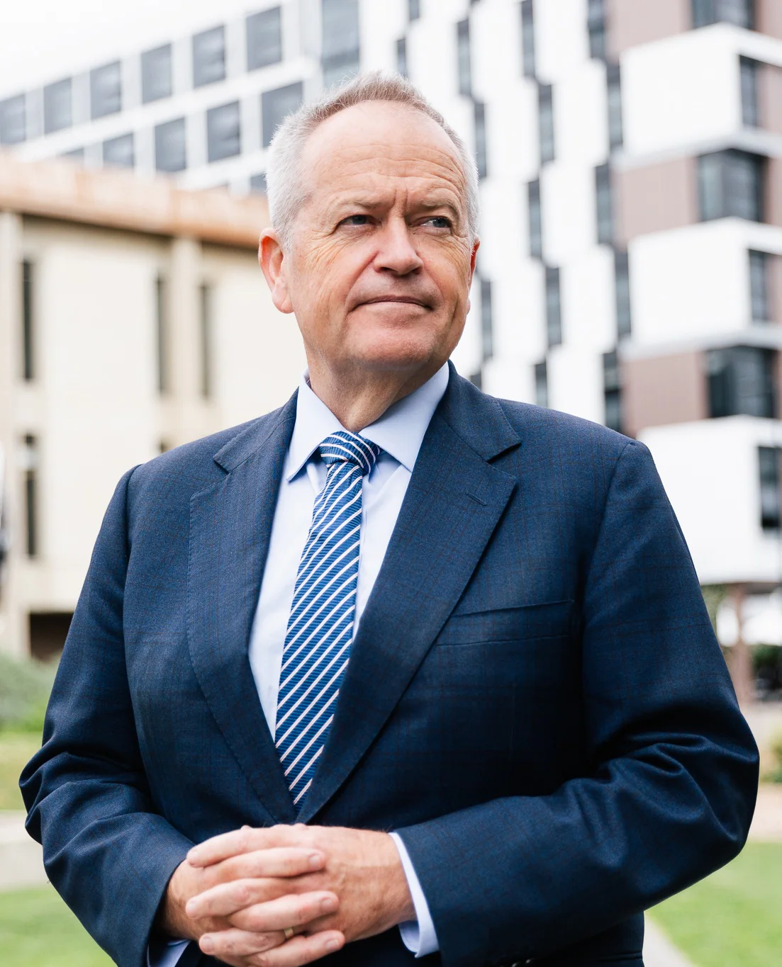 Portrait of a middle-aged man in a blue suit outdoors near modern buildings, looking to the side.