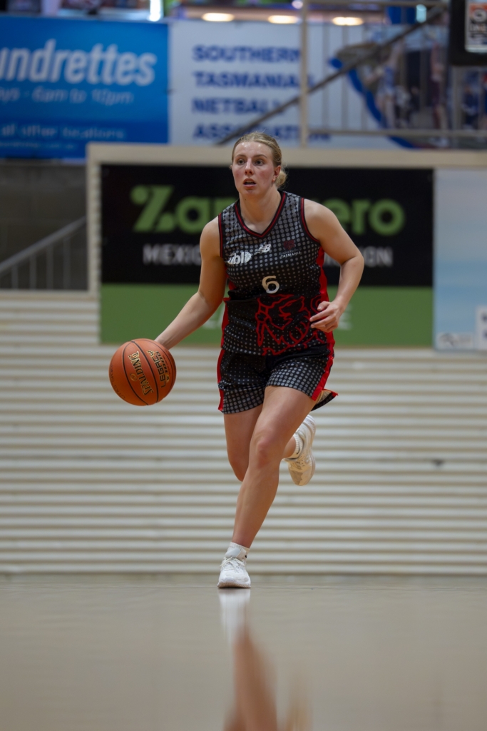 Female basketball player dribbling the ball on an indoor court, wearing a black and red uniform with number 6.