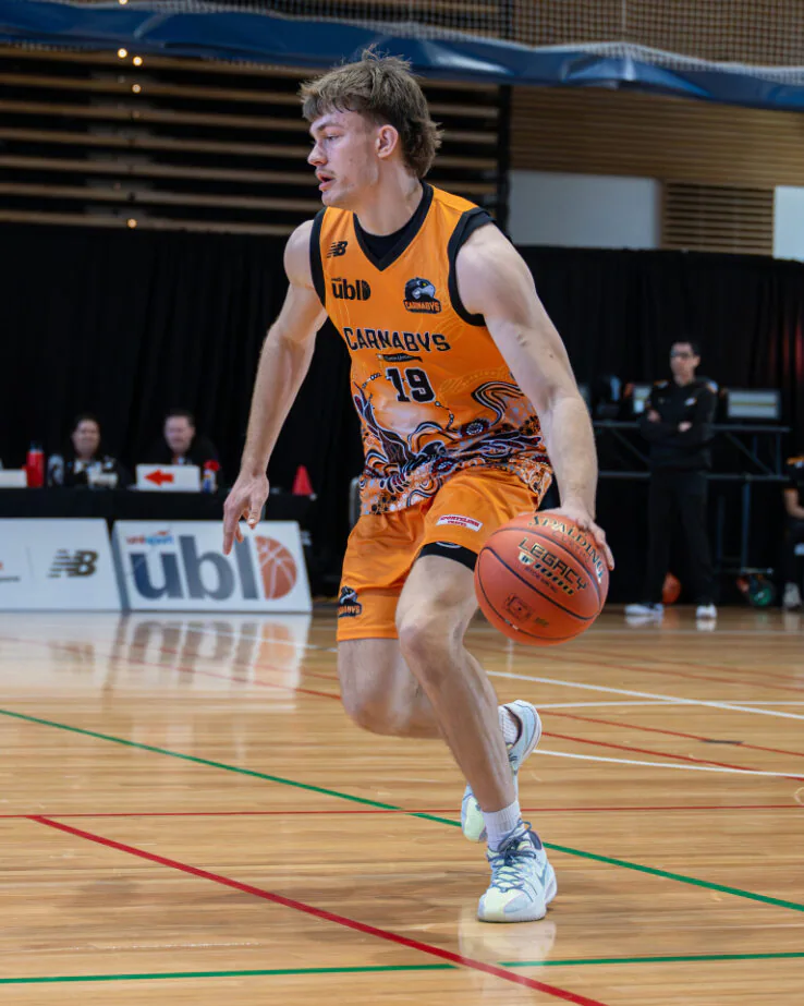 Basketball player in an orange jersey with number 19 dribbling on an indoor court during a game.