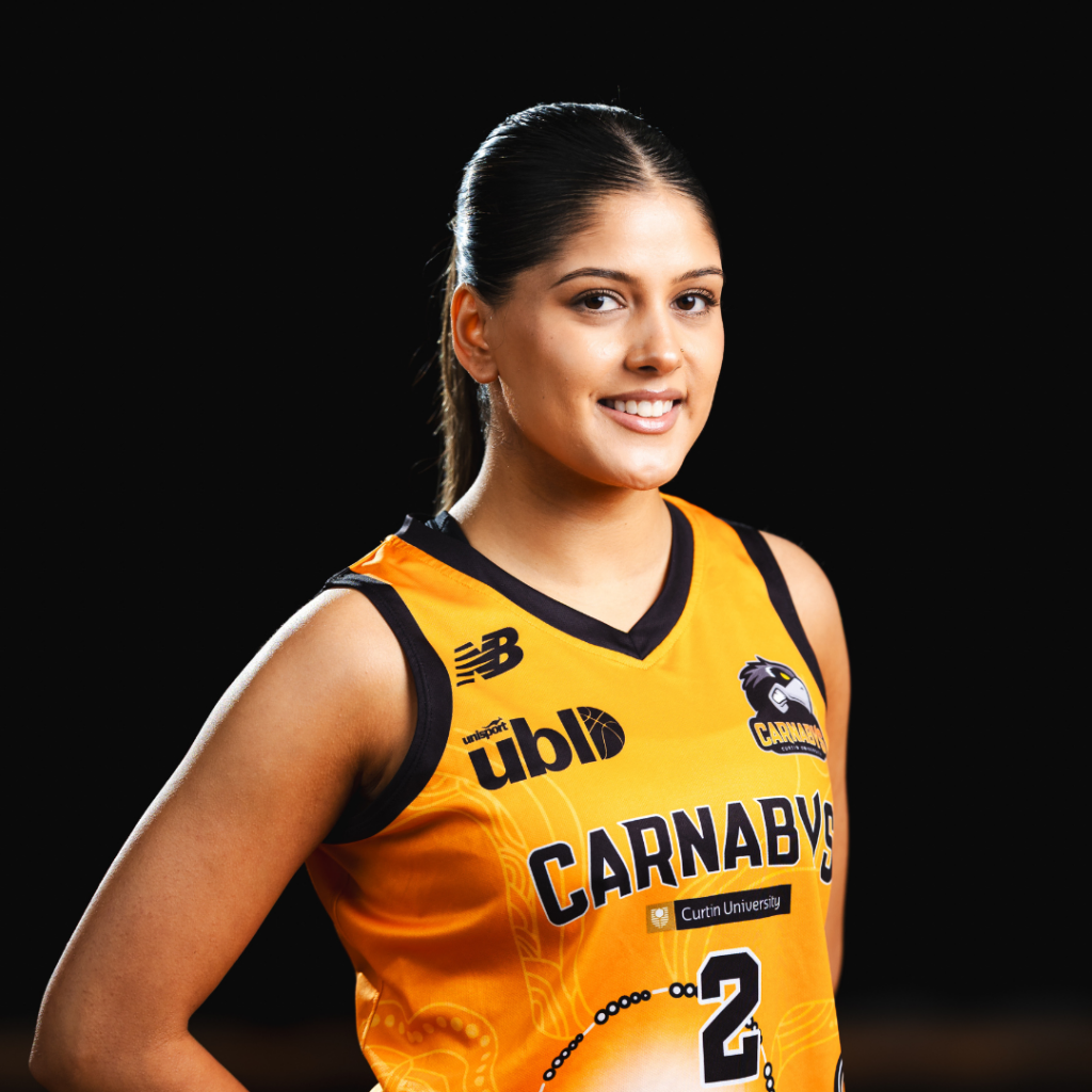 Portrait of a female basketball player in an orange Carnaby's jersey, smiling at the camera, against a dark background.