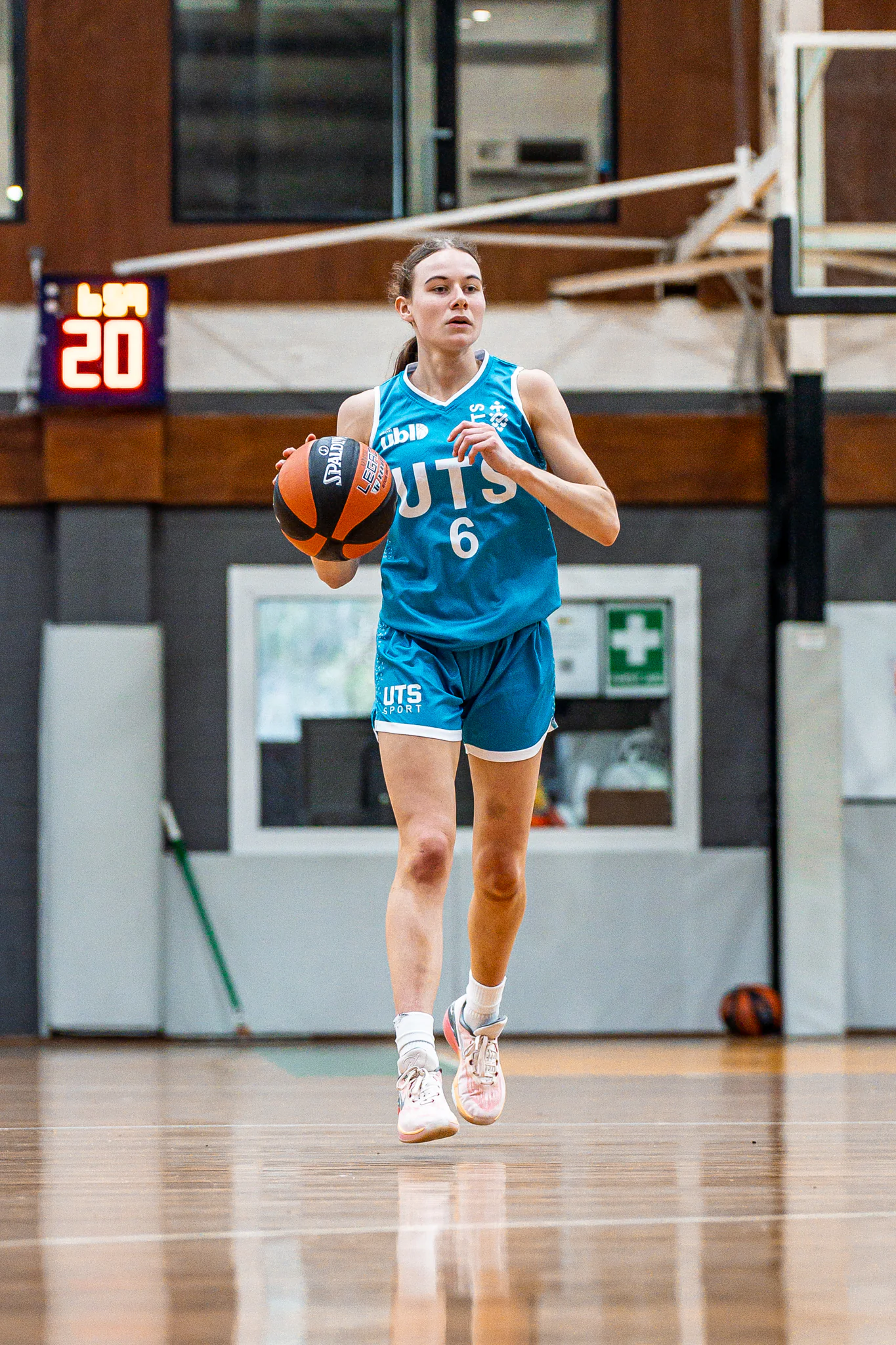 Female basketball player in a teal jersey (number 6) dribbling a basketball on an indoor court.