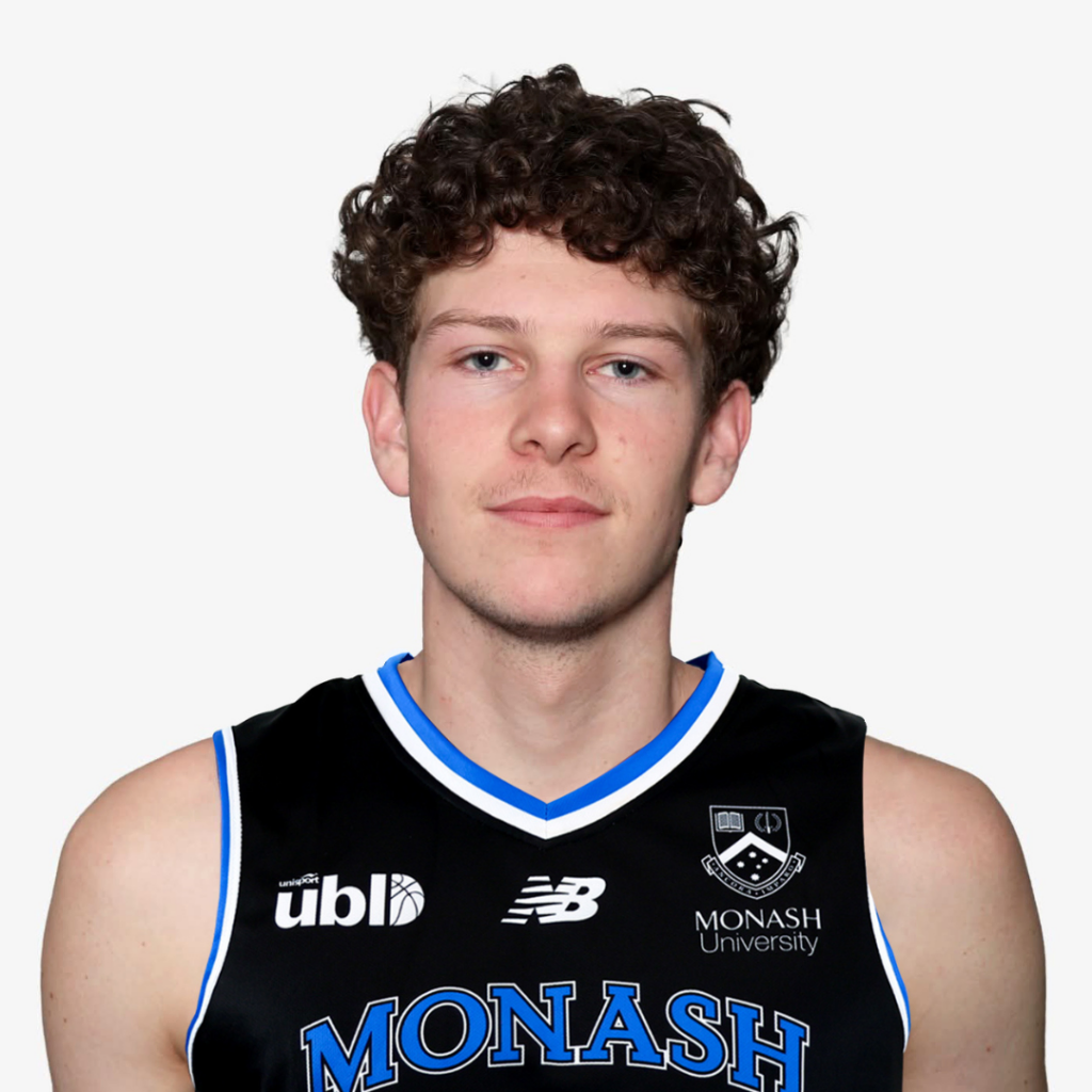 Portrait of a young man with curly brown hair wearing a black Monash University basketball jersey with blue trim and the MONASH logo visible.