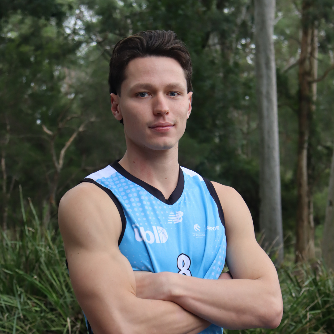 Young man in a blue sleeveless sports jersey with arms crossed, outdoors in a park.