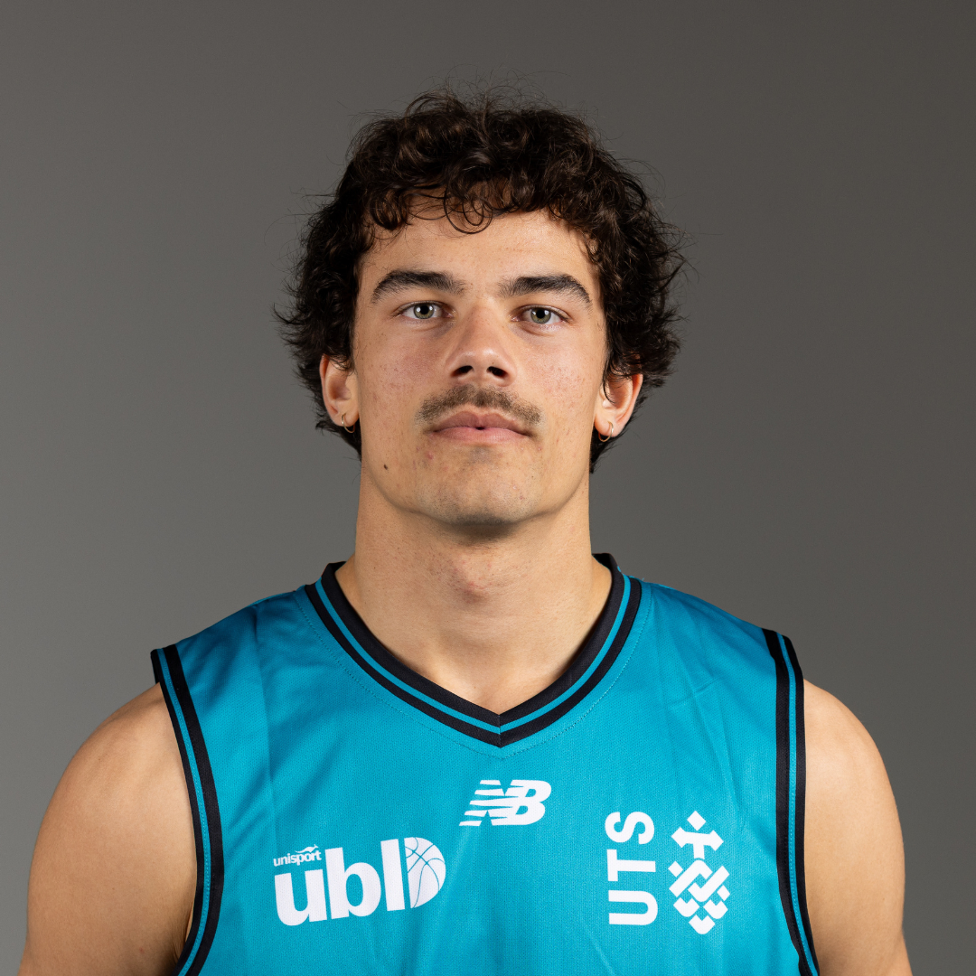 Portrait of a young man with curly dark hair wearing a turquoise basketball jersey, looking at the camera.