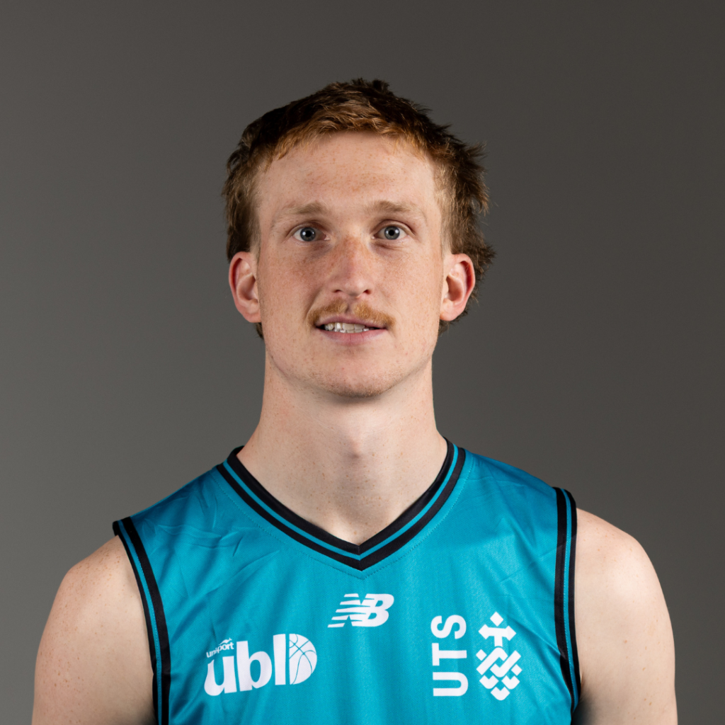 Portrait of a young man with short light brown hair wearing a teal basketball jersey, standing against a gray backdrop, facing the camera.
