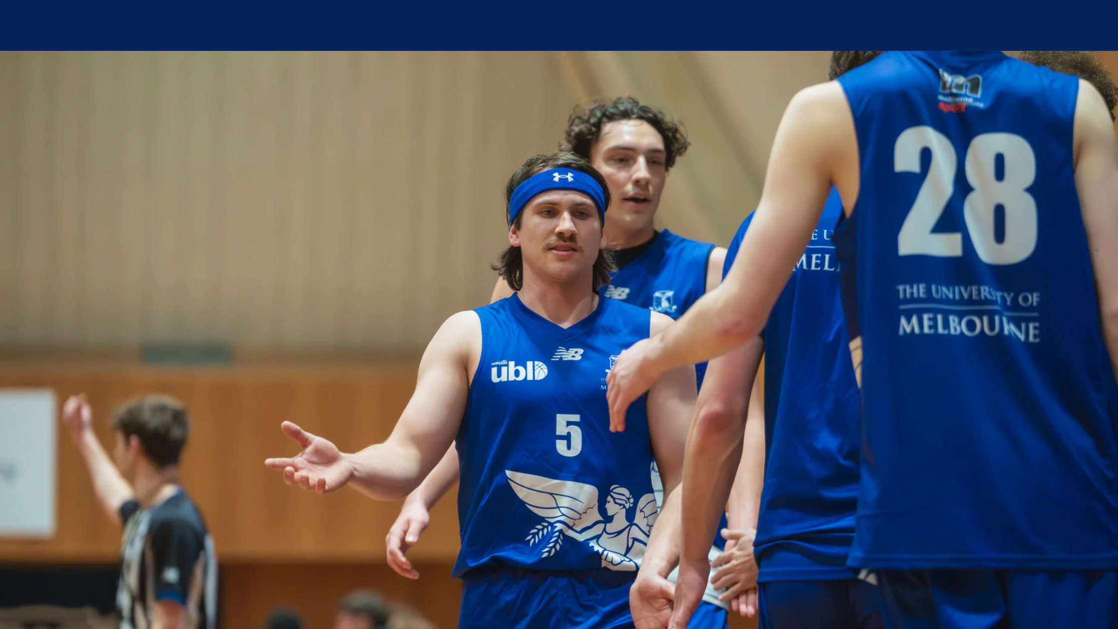 Basketball players in blue uniforms high-fiving on a court, central player wearing number 5 and a blue headband.