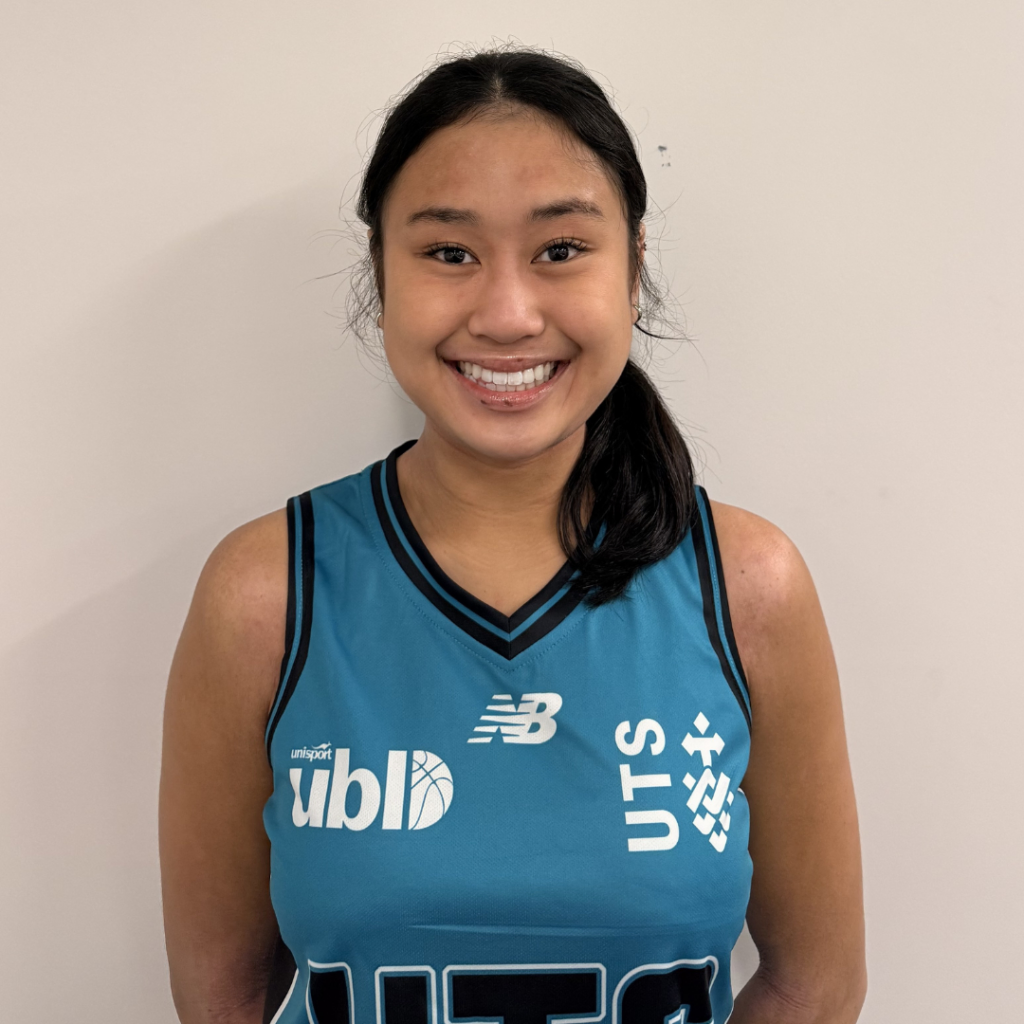 Smiling young woman in a teal basketball jersey posing against a plain wall, with team logos visible on the front.
