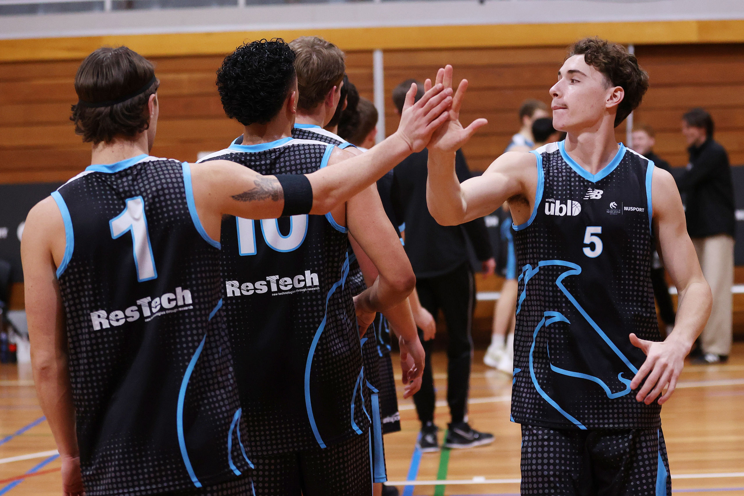 Basketball players in black and blue uniforms high-fiving on a gym court.