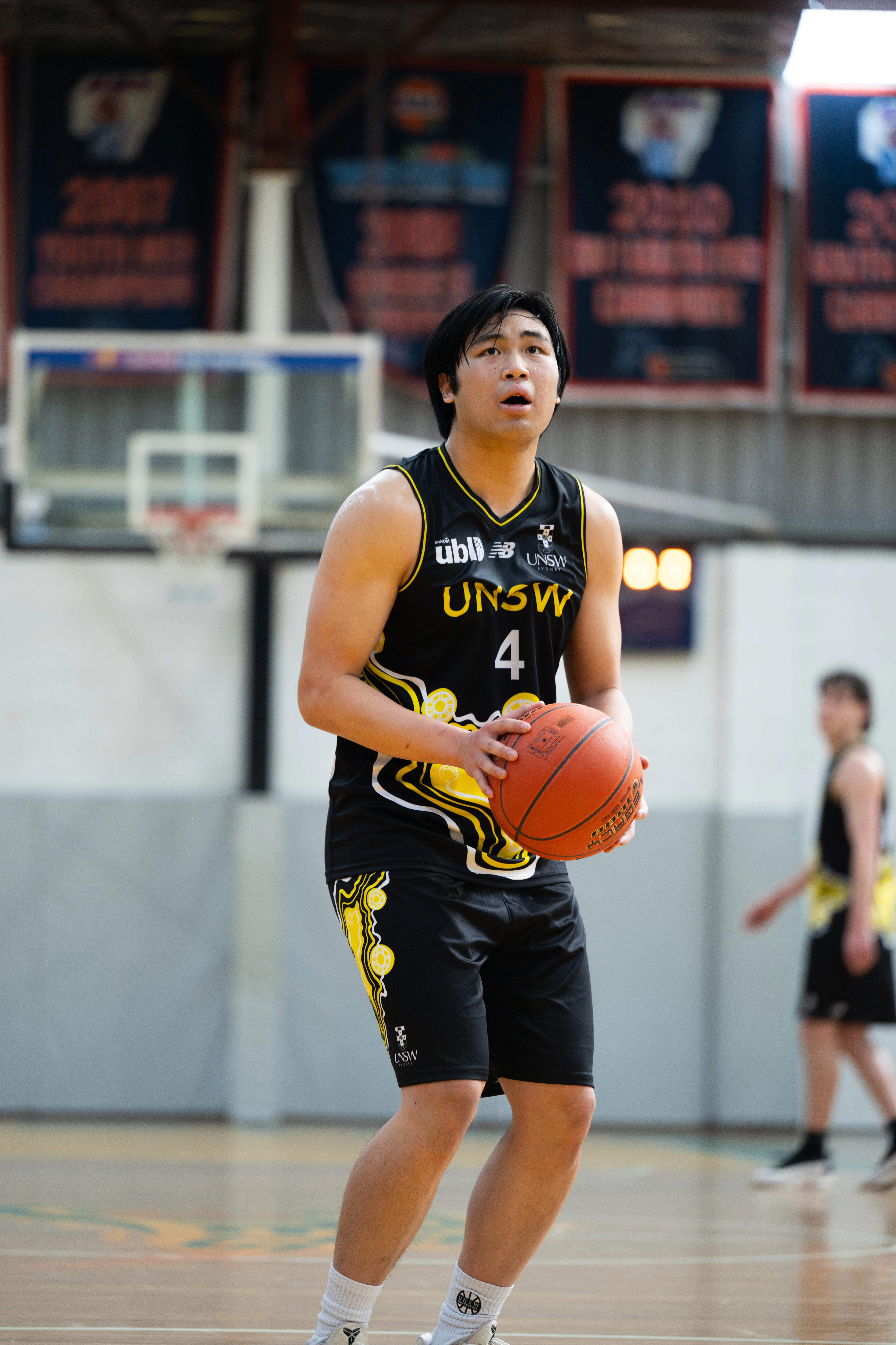 Male basketball player in black UNSW jersey holding an orange basketball on a court, ready to pass or shoot.