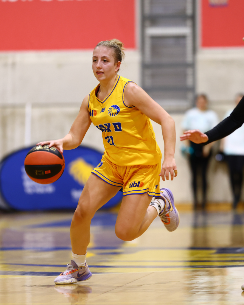 Female basketball player in yellow uniform dribbling the ball on an indoor court.