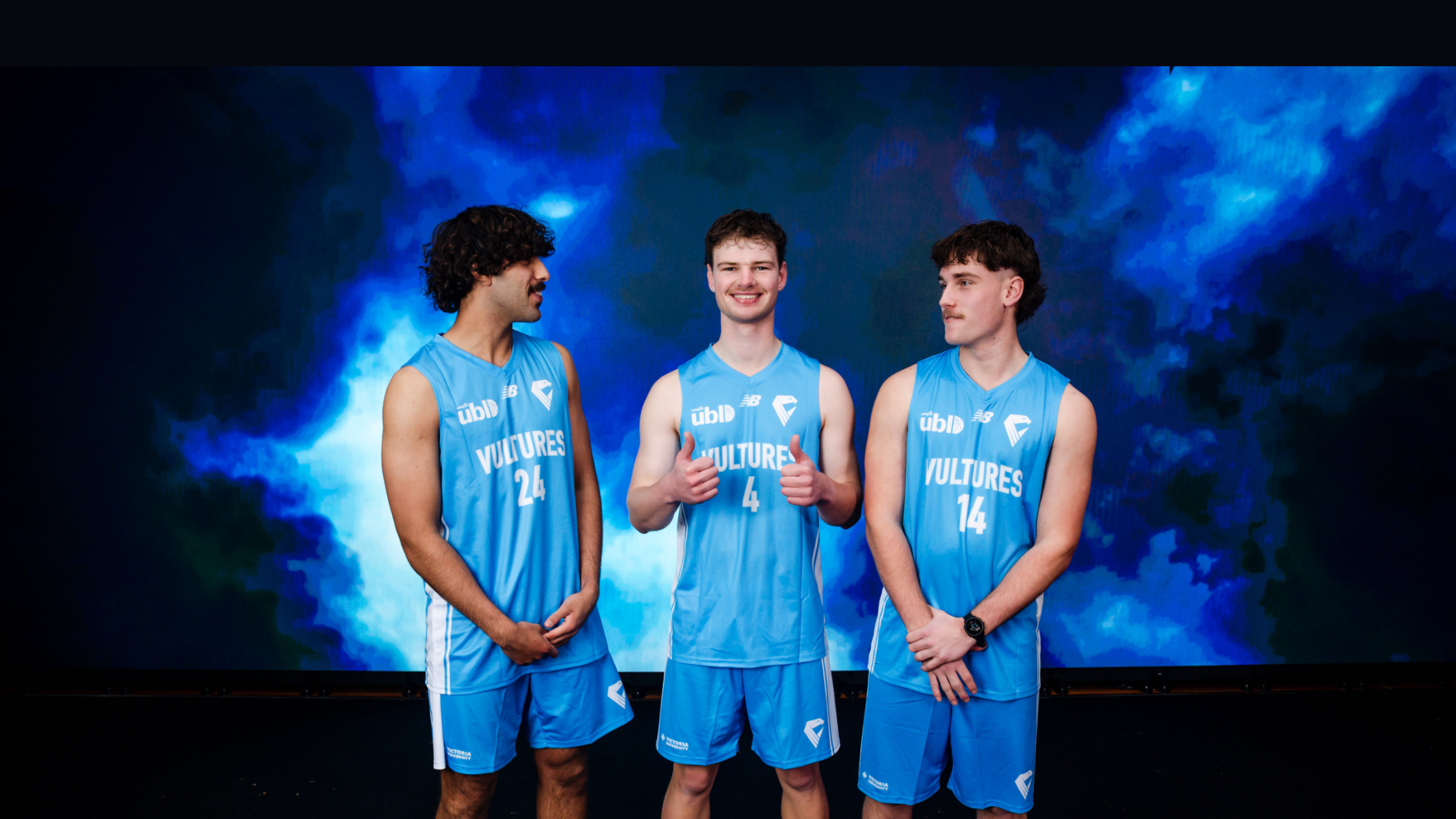 Three athletes in matching blue uniforms with 'VULTURES' on their chests, posing against a blue smoky backdrop.